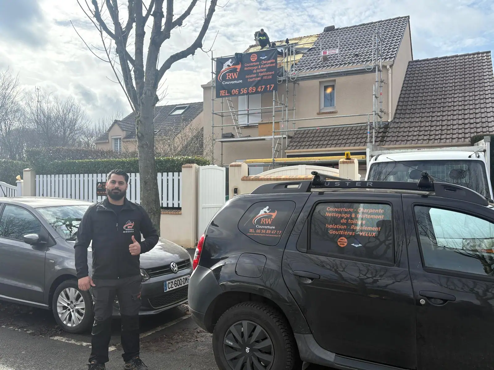 Véhicule d'intervention floqué aux couleurs de RW Couvreur, garé devant un chantier de couverture monté sur échafaudage — un couvreur travaille sur le versant